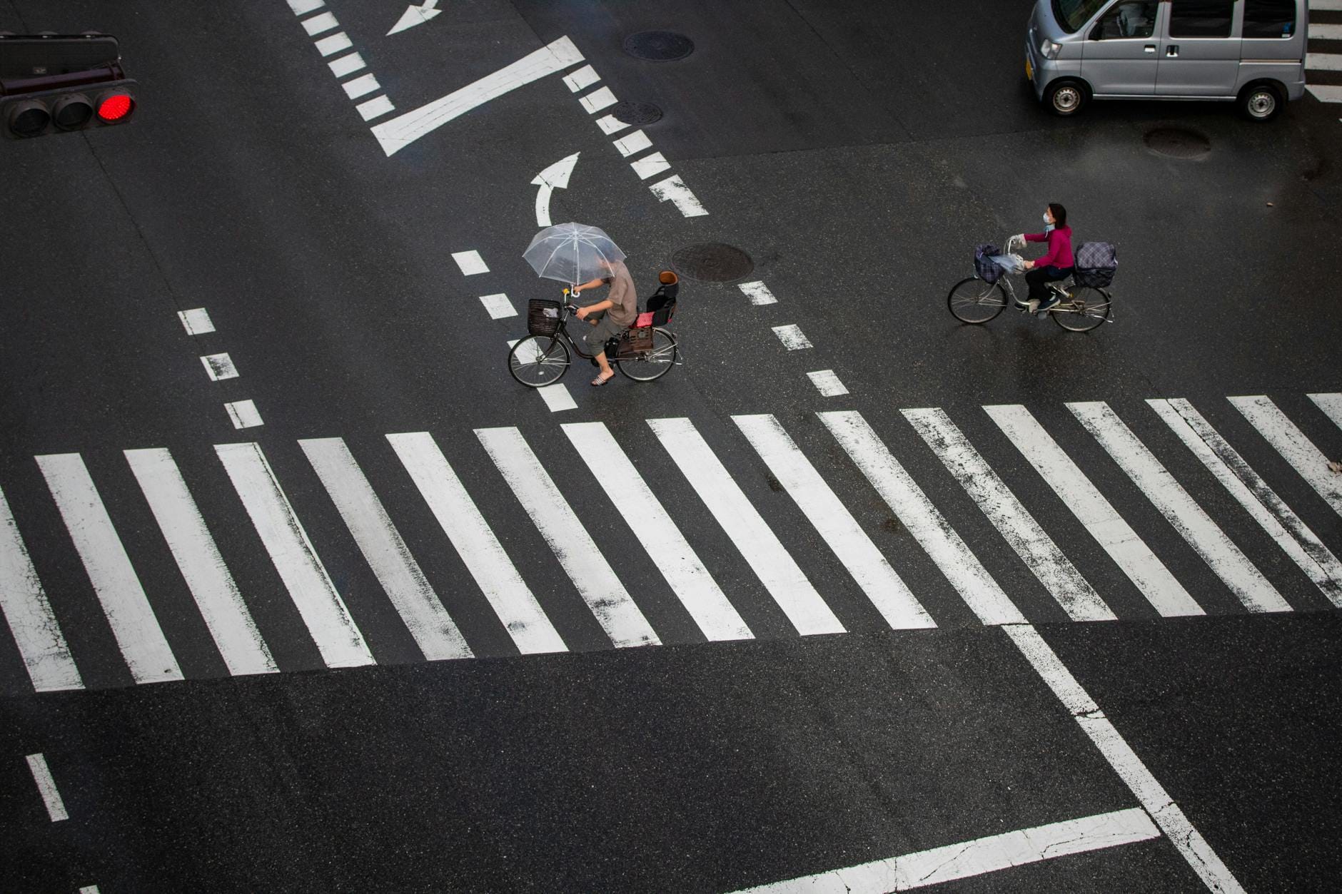 Rowerzyści z parasolami przejeżdżają przez mokre przejście dla pieszych