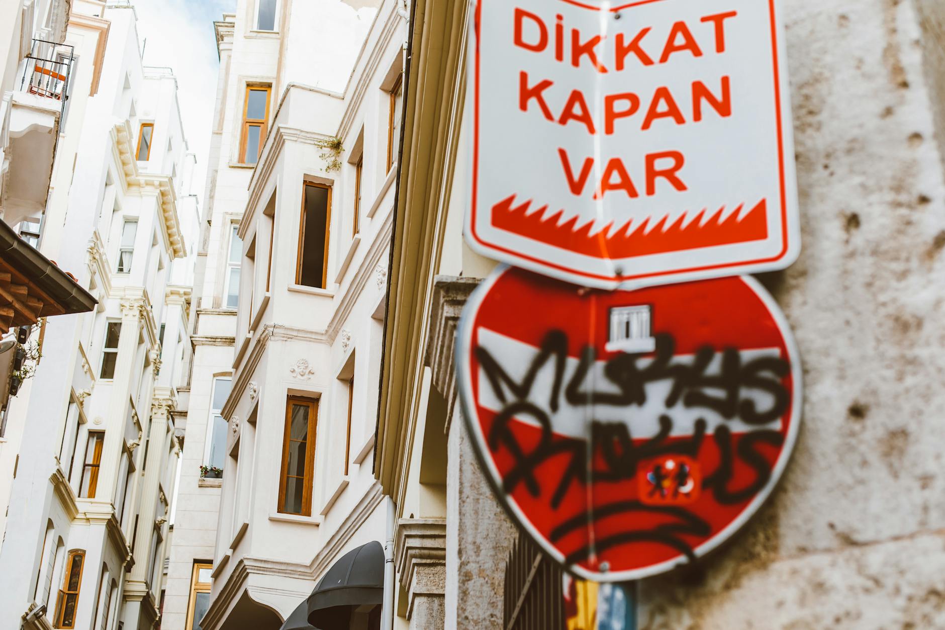 Turecki znak ostrzegawczy z graffiti na tle historycznych kamienic
