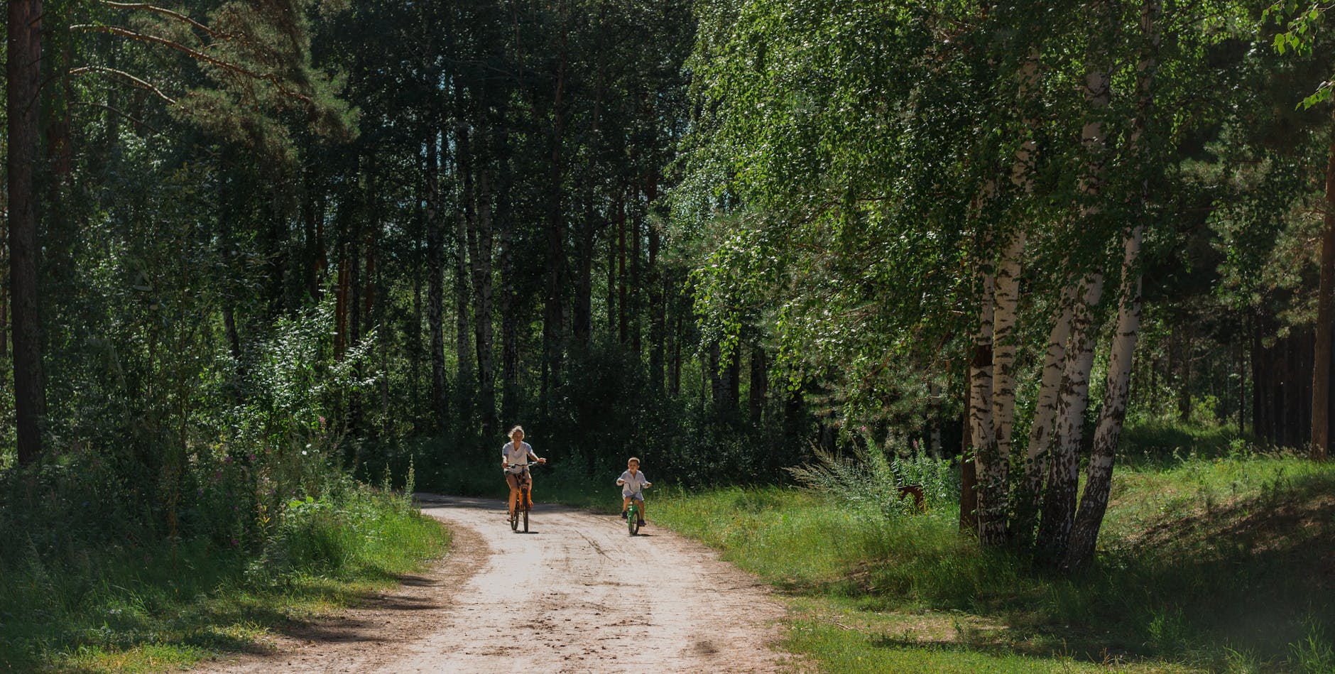 Na rower z dzieckiem: bezpieczne trasy, postoje i co spakować Mama jadąca na rowerze z dzieckiem leśną ścieżką w słoneczny dzień