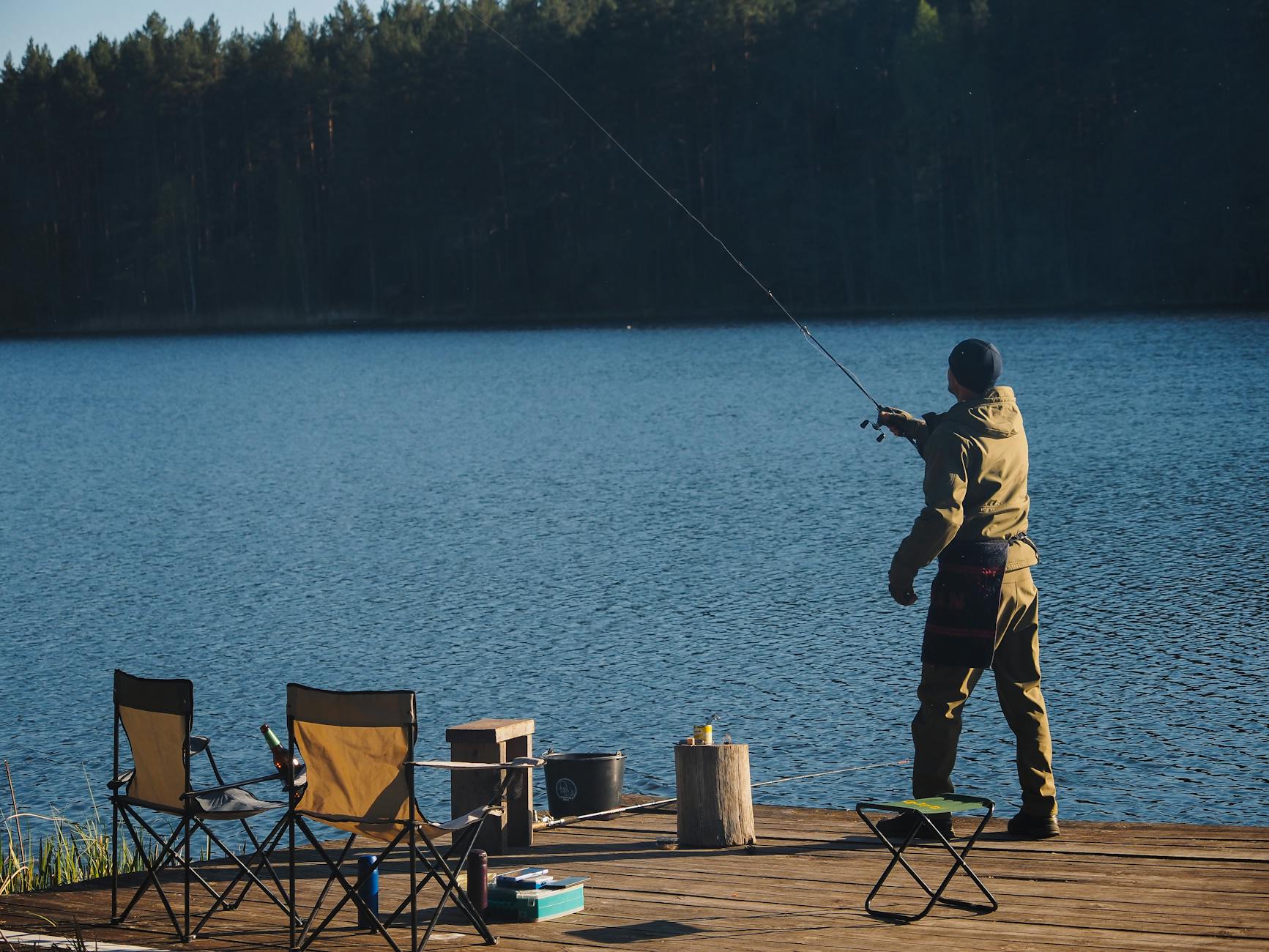 Wędkarz siedzący na pomoście nad spokojnym jeziorem z krzesłami