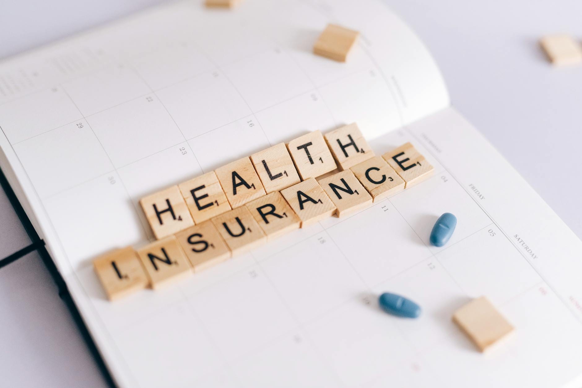 Kafelki z napisem health insurance na planerze obok tabletek