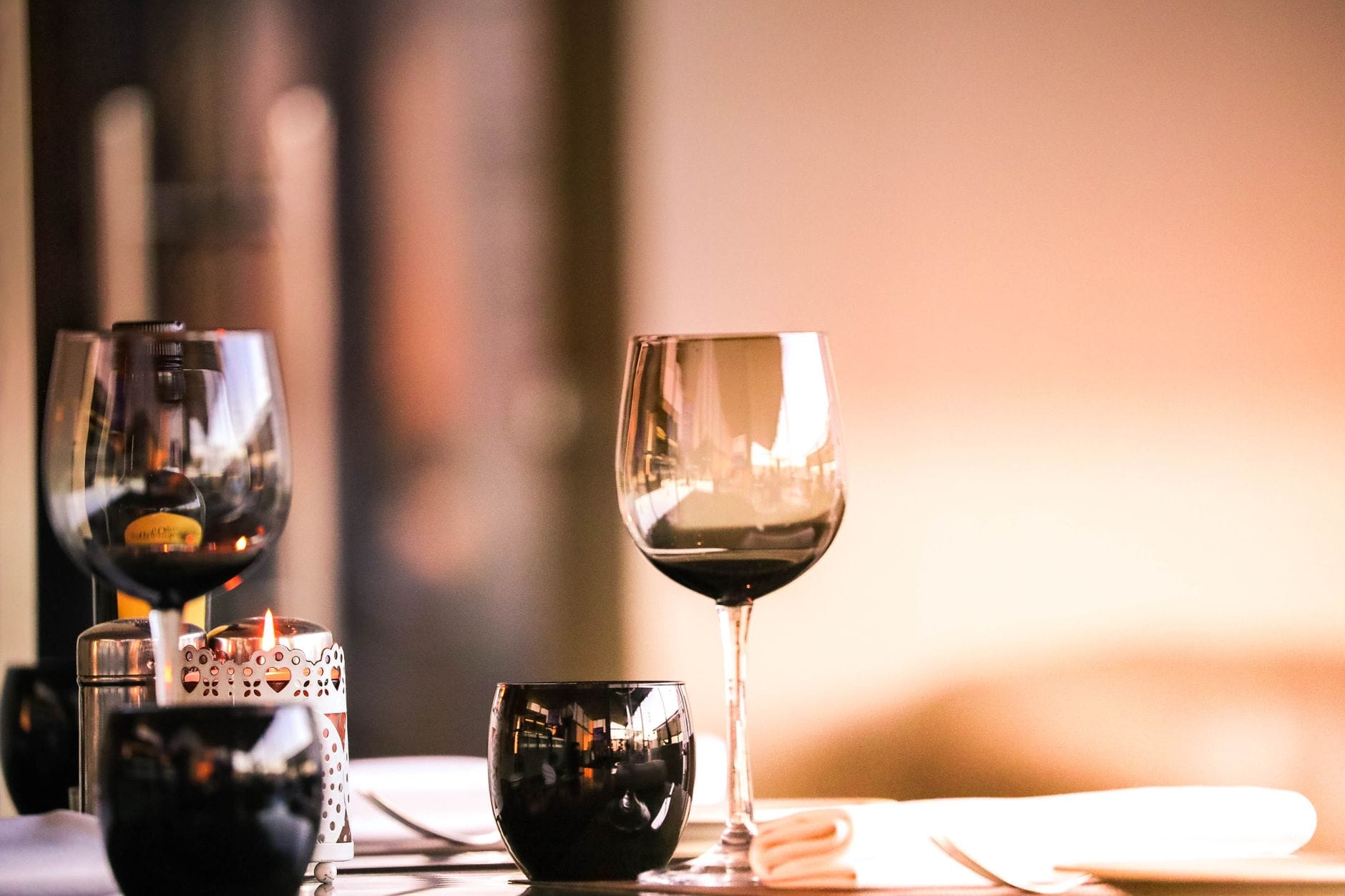 Gdzie na randkę w okolicy? Restauracje, które robią nastrój Stolik w restauracji z kieliszkami wina i zapaloną świecą, romantyczny nastrój
